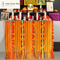 Decorative table with colorful patterned cloth, skulls, and other items on a gray background.