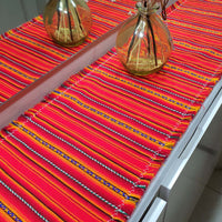 Colorful woven table runner on a table with two decorative bottles.
