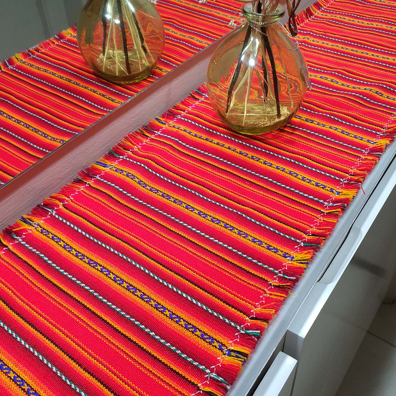 Colorful woven table runner on a table with two decorative bottles.
