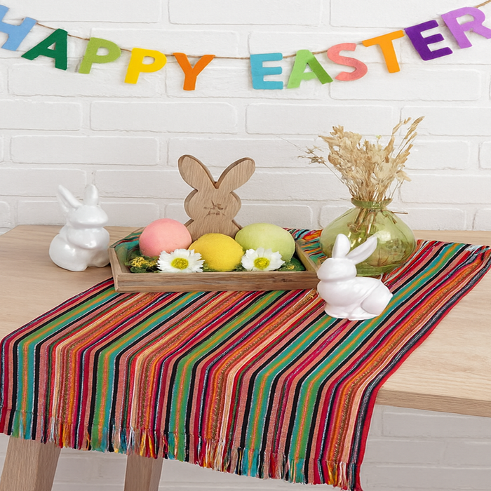 Easter-themed table setting with colorful striped tablecloth, bunny decorations, and 'Happy Easter' banner.