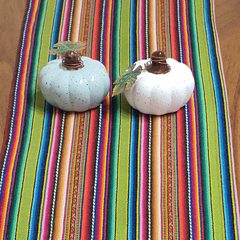 Two white pumpkins with gold stems on a colorful striped fabric background