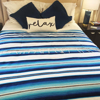 serape blanket, white, blue, on bed, with pillows and side table