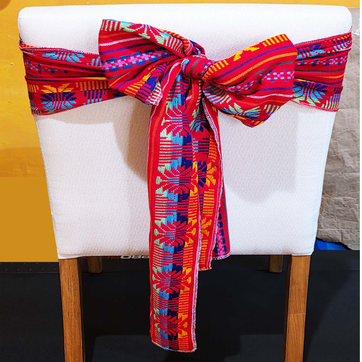 Chair with a colorful patterned sash tied around it against a yellow wall.