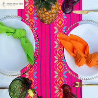 Colorful table setting with pink tablecloth, white plates, green and orange napkins, and decorative elements.