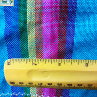 Close-up of a colorful striped woven fabric with a yellow ruler showing measurement markings to indicate scale.