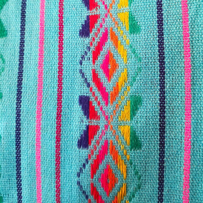A close-up of a woven textile featuring a turquoise base with vertical stripes and a central geometric diamond pattern in pink, orange, yellow, green, and purple.
