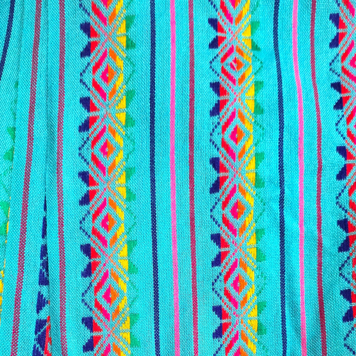 A close-up of a turquoise blue woven textile with vertical stripes and colorful geometric diamond patterns in pink, yellow, orange, green, and dark blue.
