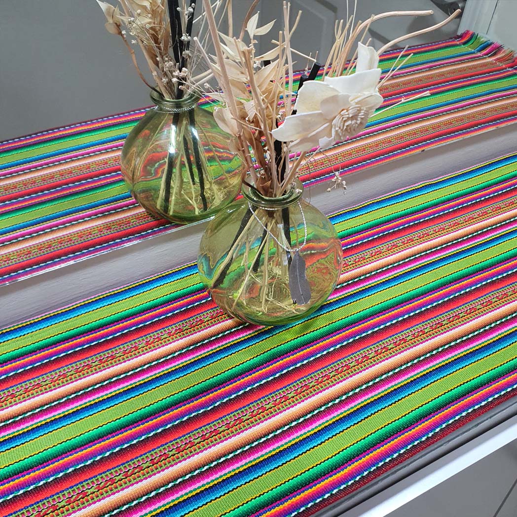 Colorful striped table runner with two glass vases containing dried plants on a table.
