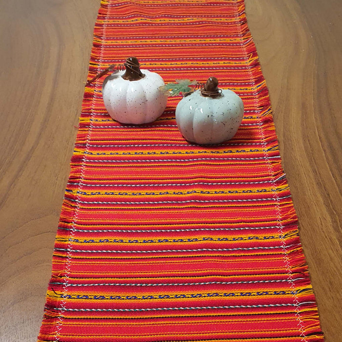 Colorful striped table runner with two small pumpkins on a wooden surface
