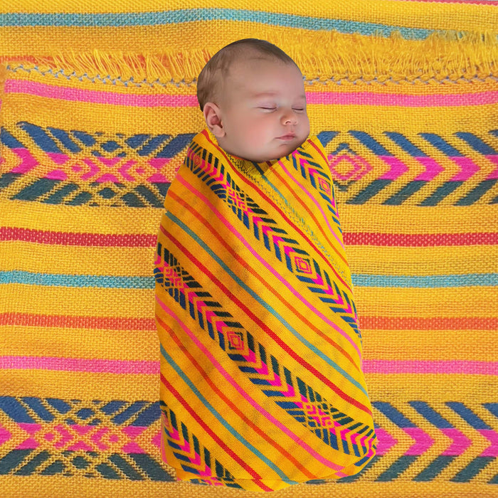 Newborn baby swaddled in a colorful blanket on a patterned yellow background