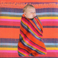 Baby swaddled in a colorful striped blanket on a multicolored fabric background
