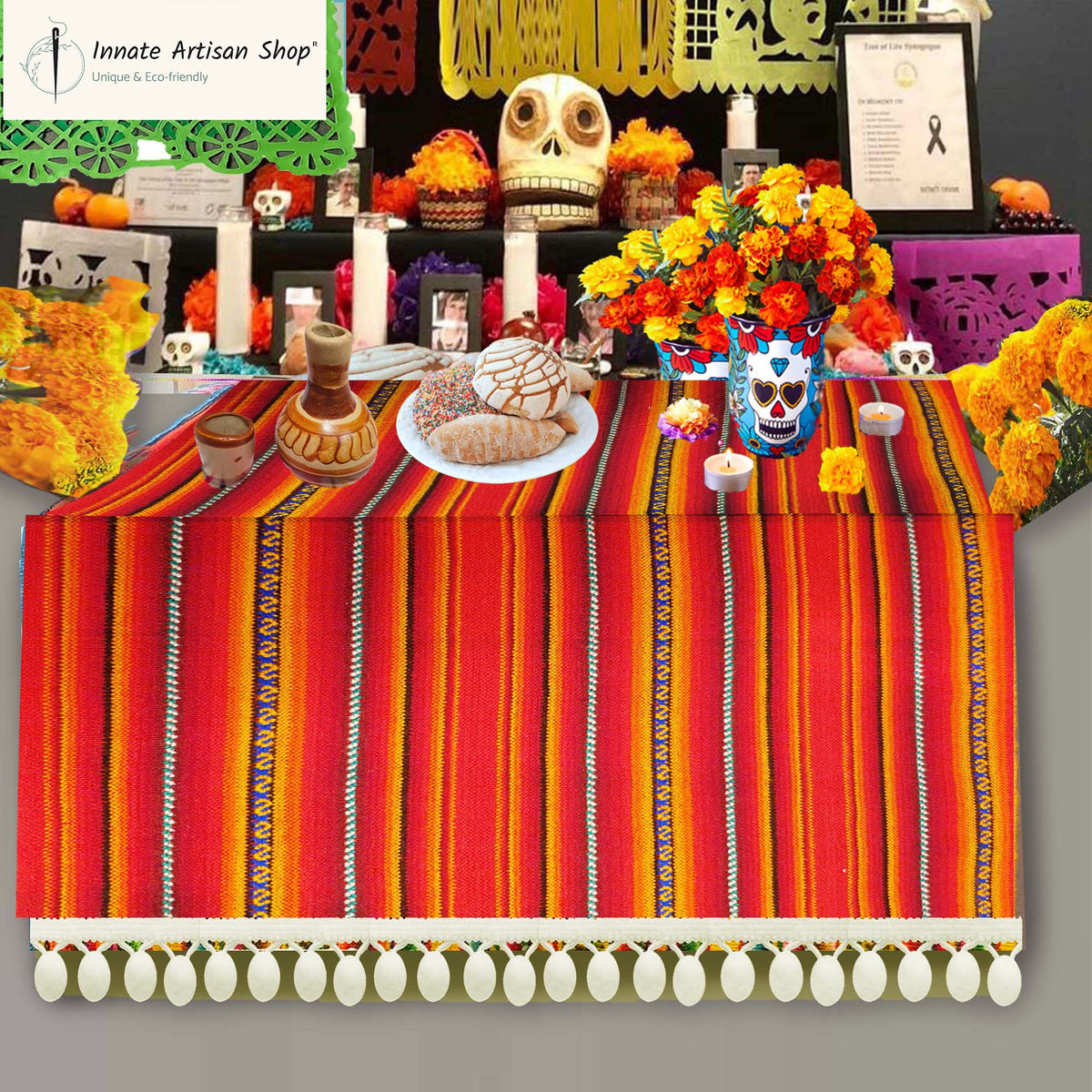 Decorative table setup with colorful striped tablecloth, flowers, and skeleton decorations on a gray background.