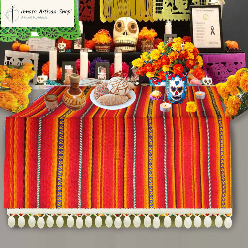 Decorative table setup with colorful striped tablecloth, flowers, and skeleton decorations on a gray background.