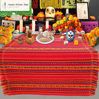 Decorative table setup with colorful tablecloth, flowers, and skull decorations on a gray background.