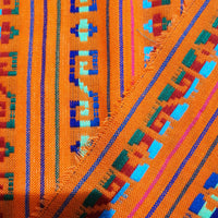 Close-up of colorful woven fabric with geometric patterns on an orange background