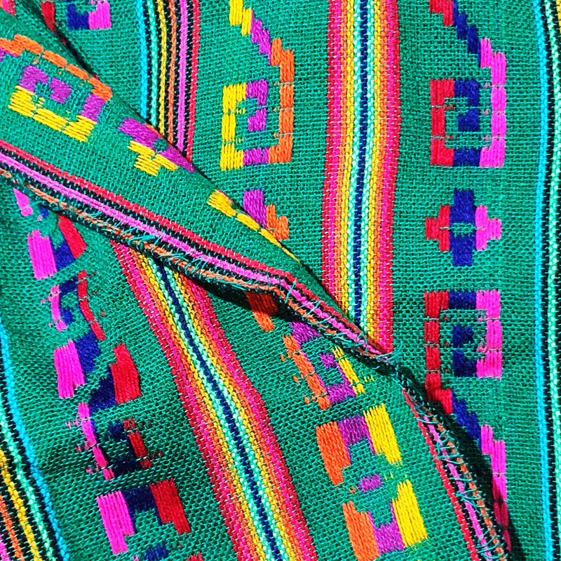 Close-up of a colorful woven fabric with geometric patterns on a teal background.