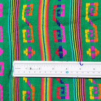 Colorful fabric with geometric patterns and a ruler for scale on a green background