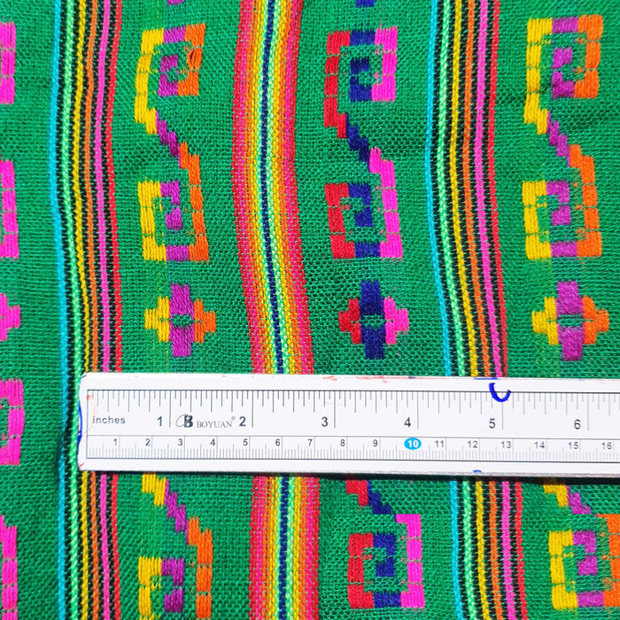 Colorful fabric with geometric patterns and a ruler for scale on a green background