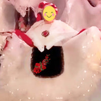 Close-up of a person wearing a white outfit with red accents and floral decorations, surrounded by a snowy background.