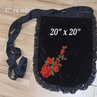 Black velvet bag with red floral embroidery on a wooden floor