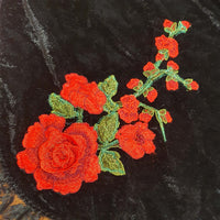 Embroidered red roses with green leaves on a black fabric background