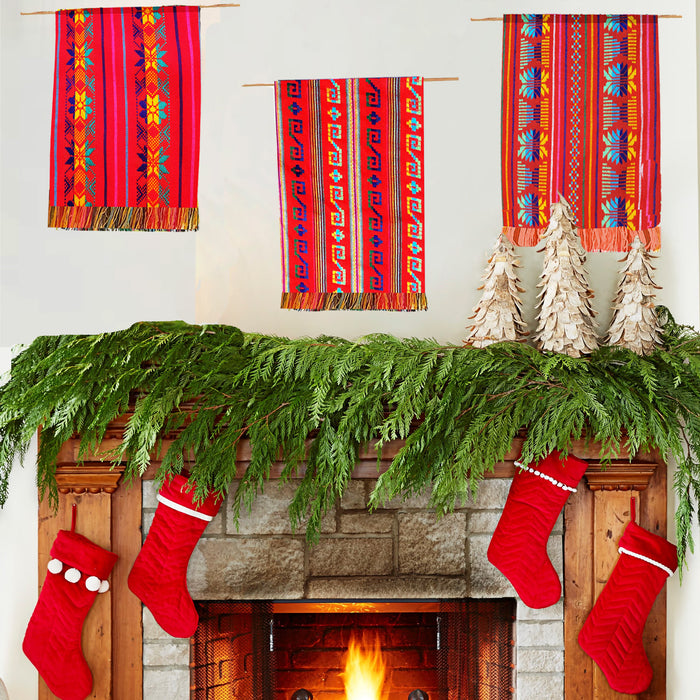 Decorative mantel with red patterned scarves, greenery, and red stockings in front of a fireplace.
