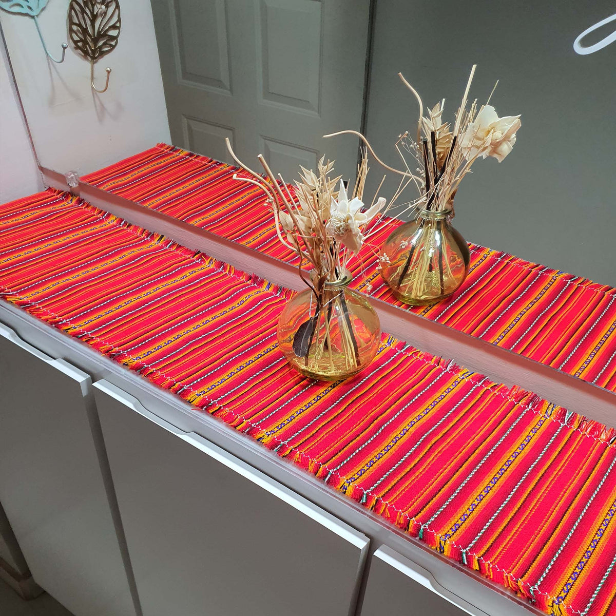 Orange striped table runner with gold vases and decorative plants on a table.
